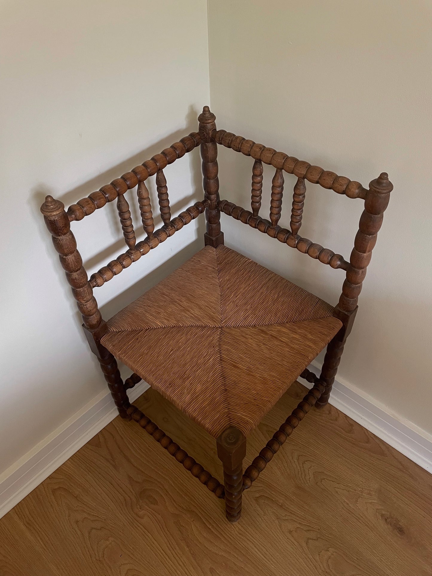 Wooden corner chair with woven seat in a corner of a room.