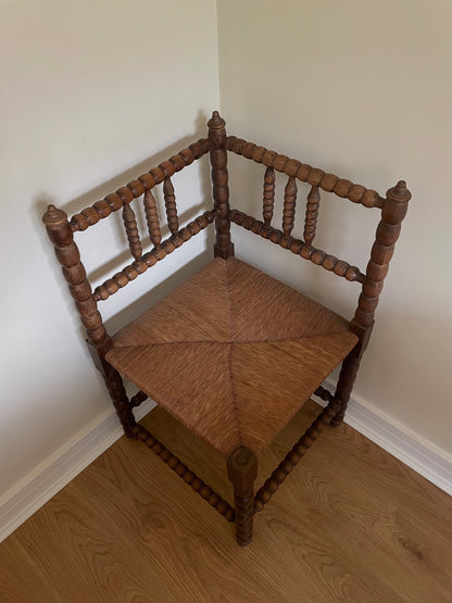 Wooden corner chair with woven seat in a corner of a room.