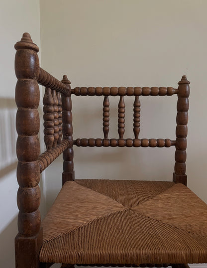 Wooden chair with spindle back and woven seat against a plain wall